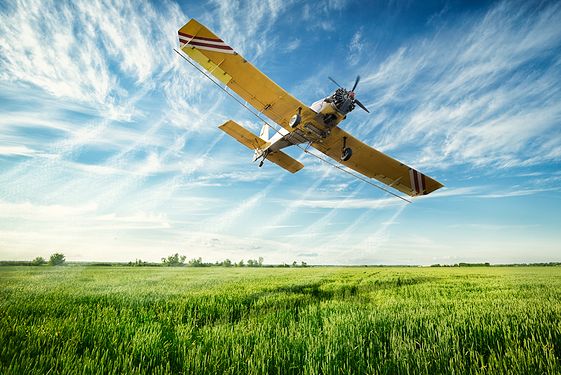 Yellow plane flying over green field